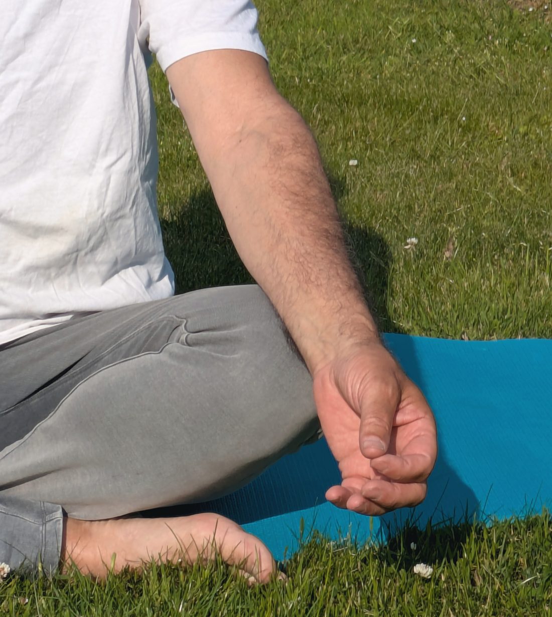 Händer i meditationsställning på yogamatta i gräset.